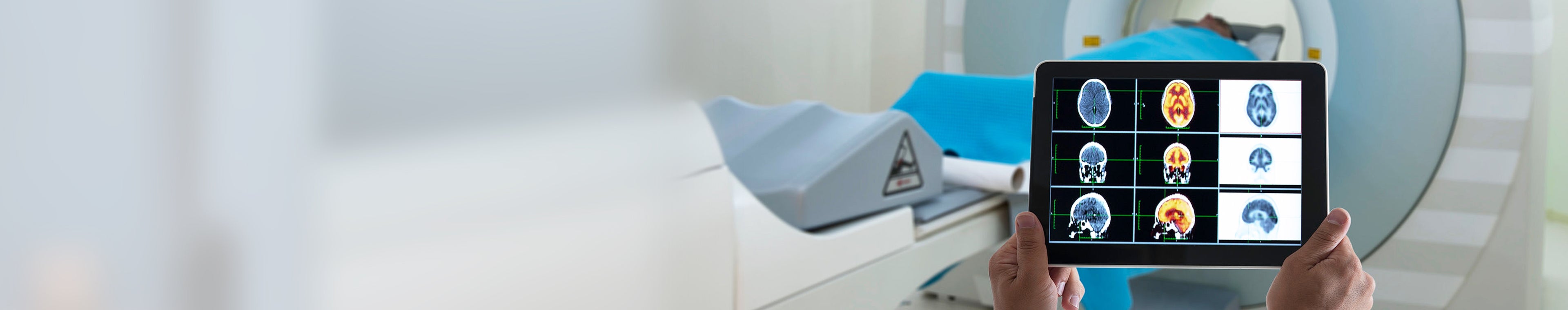 Doctor viewing an MRI on a tablet while standing in front of the patient laying inside the MRI