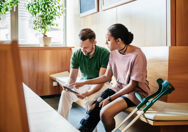 Person in leg brace looking over medical report with medical practitioner 