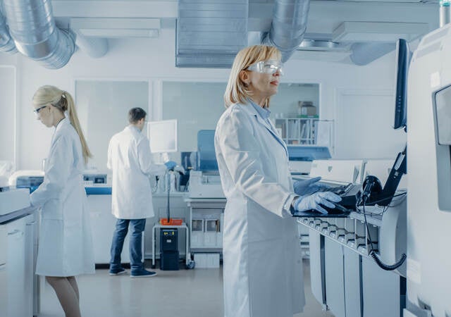 Team of Research Scientists Working On Computer, with Medical Equipment, Analyzing Blood and Genetic Material Samples with Special Machines in the Modern Laboratory.