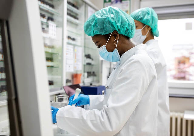 Two scientists making medicine at a laboratory. Doctors working together at pharmacy lab wearing protective work wear.