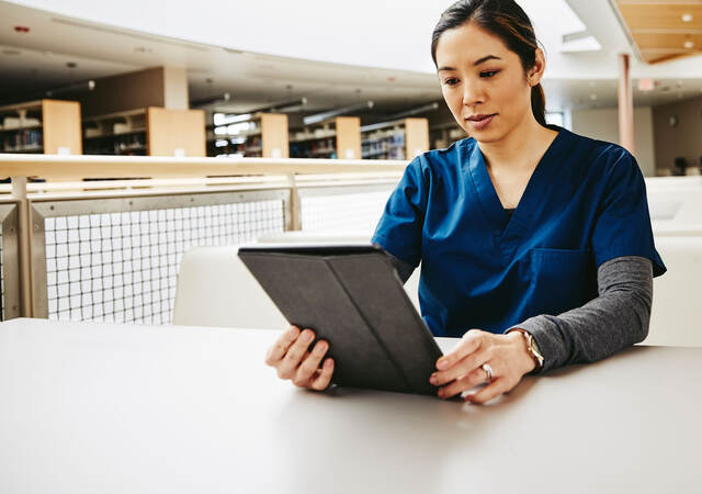 Medical student reading tablet in a library