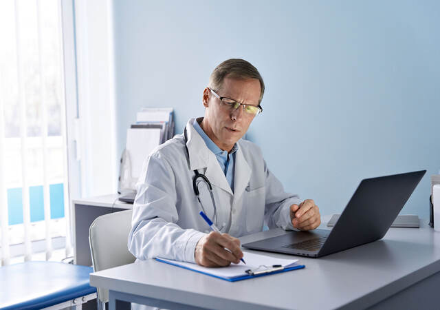 A doctor working on a laptop and taking notes