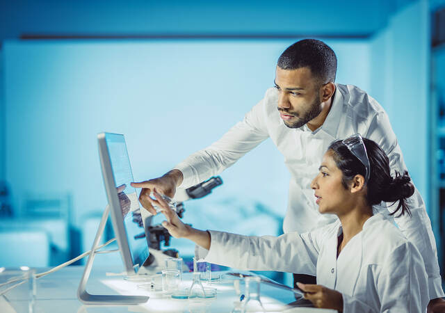 Two lab technicians pointing to data on a computer