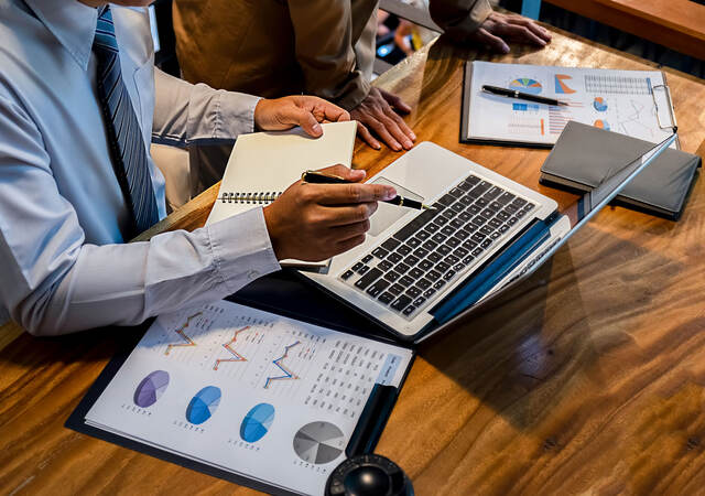 Person sitting at a desk taking notes and looking at a laptop