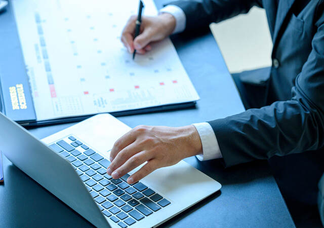 A person in a suit is taking notes and working on a laptop