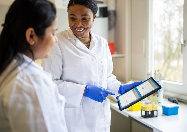 Lab technician smiling and pointing to a tablet