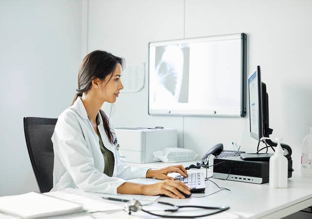 Confident doctor using computer at desk. A medical professional is working in clinic. They are wearing lab coat.