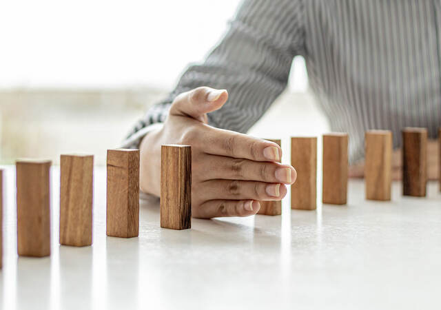 Dominos standing on a table with a hand in between two of the dominos