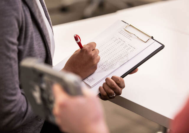 Person taking notes on a clipboard while someone tests a medical device