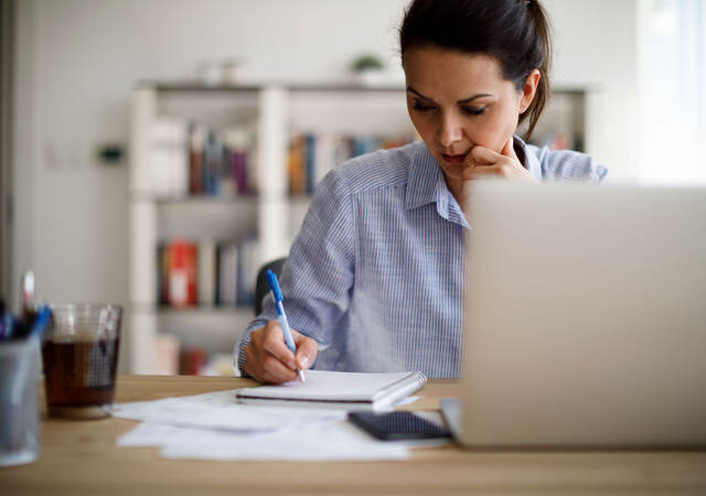 Person writing something down while working on a laptop