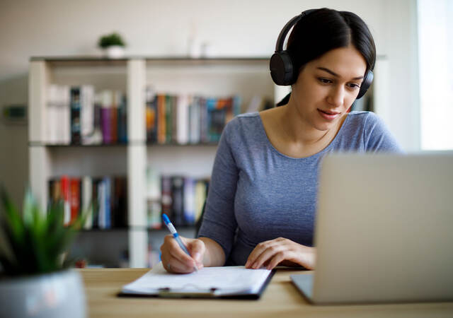 Woman with headphones taking notes and looking at a laptop