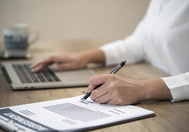 Person working at a laptop while checking a clipboard.