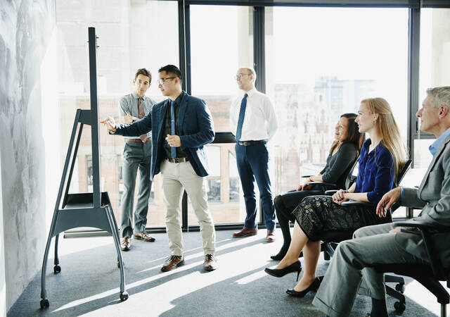 Group of colleagues having a meeting while one presents on a board