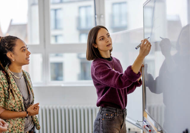 Two business colleagues collaborating while one writes on a whiteboard