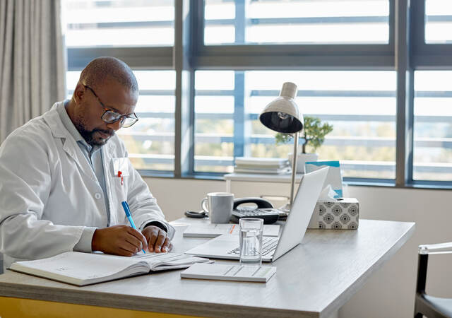 Doctor taking notes while taking an online class in an office