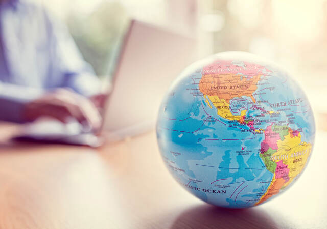 Close of a little globe with a person using a laptop in the background