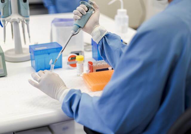 Scientist using a pipet while holding a vial