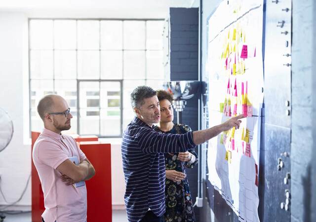 Three coworkers collaborating together in front of a whiteboard covered in post-it notes