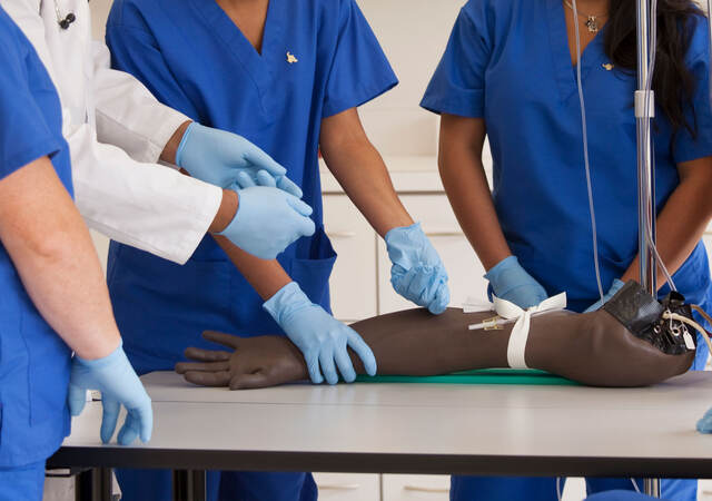 A doctor teaches a group of nursing students how to insert an IV into a fake arm