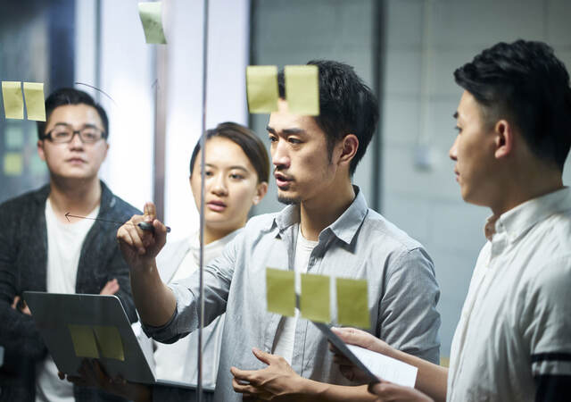 A group of colleagues collaborating with post-it notes and writing ideas on a glass wall