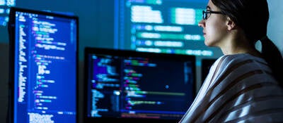 Person sitting in front of giant monitors while coding in a dark room