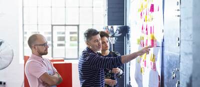 Three coworkers collaborating together in front of a whiteboard covered in post-it notes