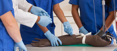 A doctor teaches a group of nursing students how to insert an IV into a fake arm