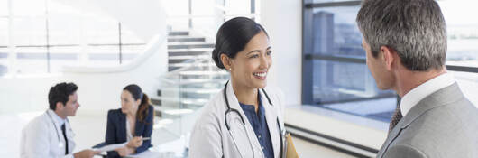 A doctor shaking hands with a business professional while another doctor has a meeting in the background