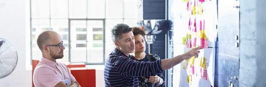 Three coworkers collaborating together in front of a whiteboard covered in post-it notes