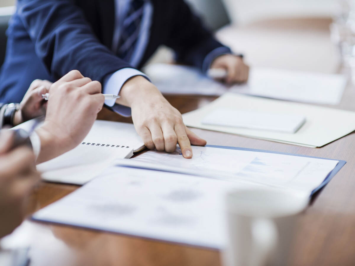 Person in a suit pointing to reports laying on a conference table during a meeting