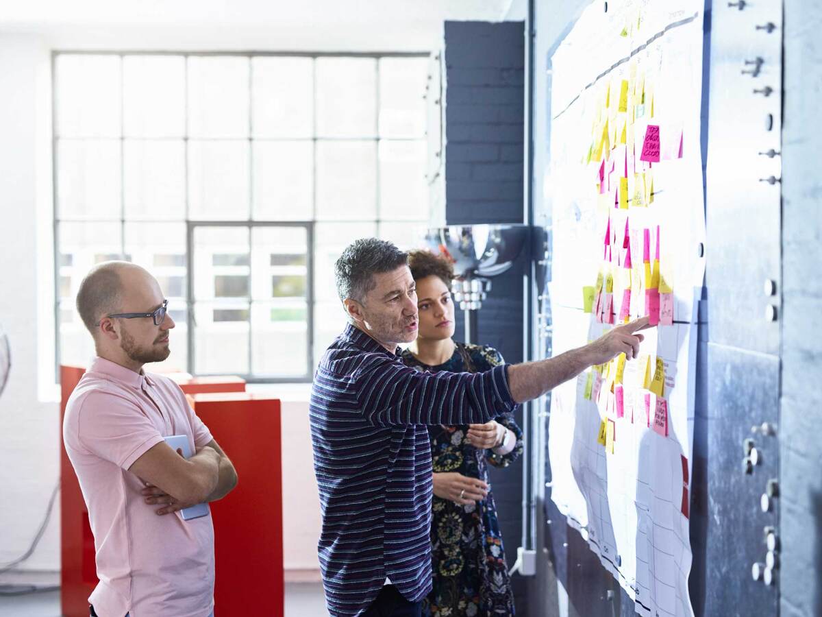 Three coworkers collaborating together in front of a whiteboard covered in post-it notes