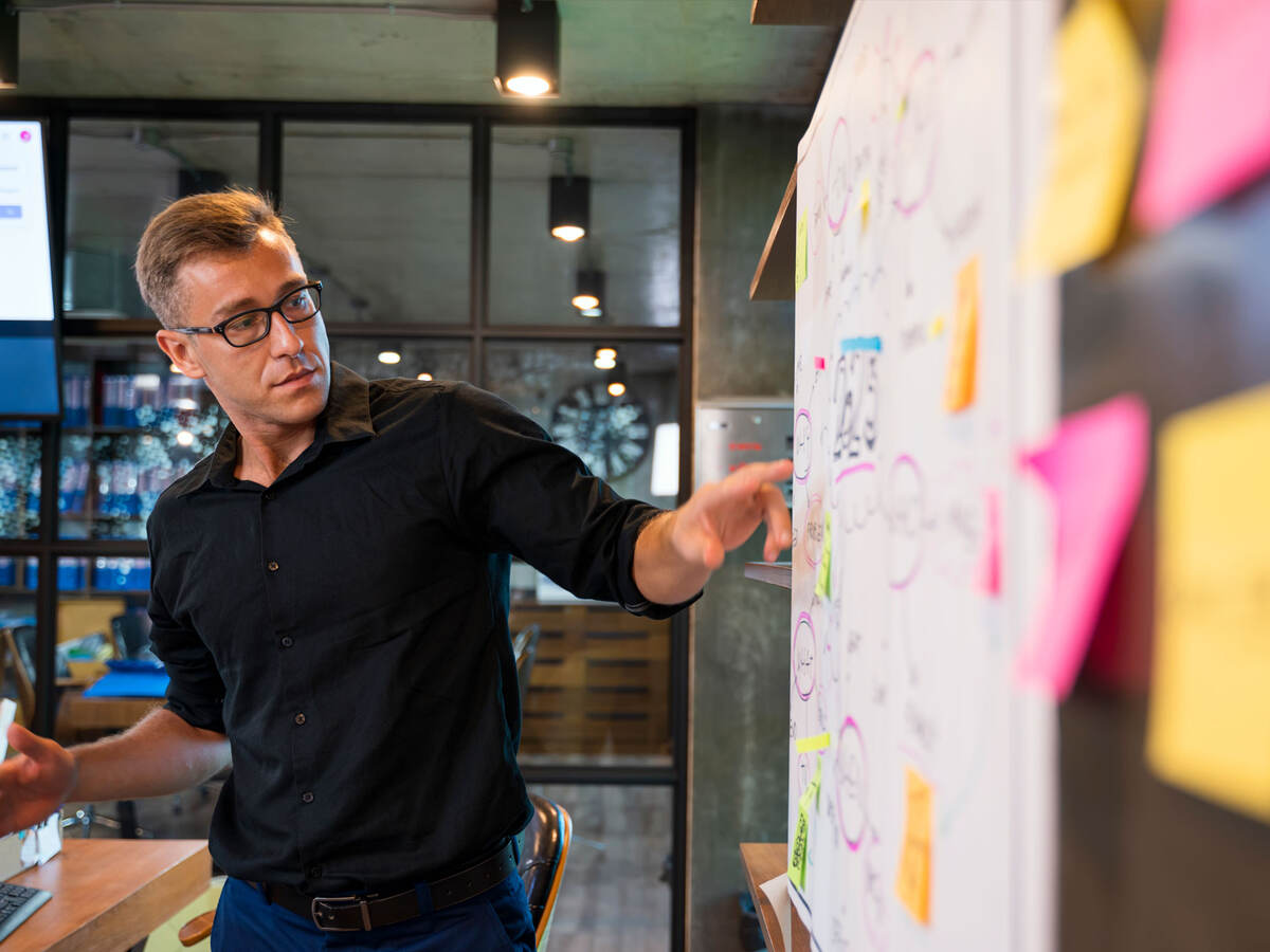 Person pointing at a whiteboard with lots of post-its on it