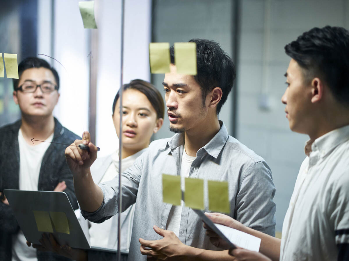 A group of colleagues collaborating with post-it notes and writing ideas on a glass wall