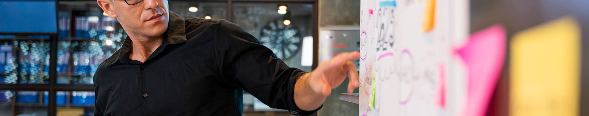 Person pointing at a whiteboard with lots of post-its on it